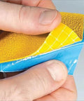 Close-up of hands peeling yellow reflective tape showing texture and adhesive backing, Slip Resistant Sensory Path And Safety Tape For Outdoors.