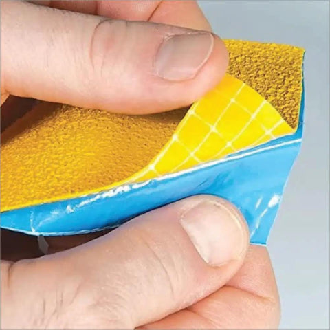 Close-up of hands peeling yellow reflective tape showing texture and adhesive backing, Slip Resistant Sensory Path And Safety Tape For Outdoors.