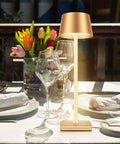 Cordless Table Lamp With Dimmable And Rechargeable Battery, Waterproof Gold Lampshade, placed on outdoor dining table with flowers