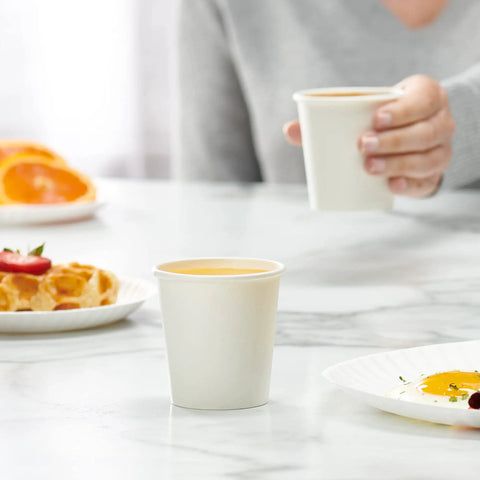 Person holding 6 Oz White Paper Cups 300 Count Small Disposable Cups for Espresso Tea Tastings Mouthwash, breakfast setting.