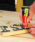 Loctite PL Premium polyurethane construction adhesive, 4 oz squeeze tube, applied to wooden letters on a wood board