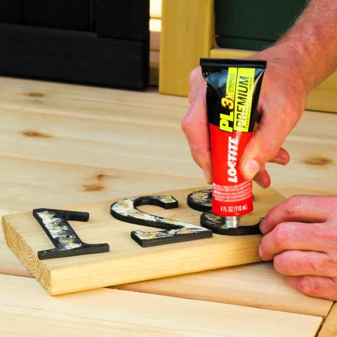 Loctite PL Premium polyurethane construction adhesive, 4 oz squeeze tube, applied to wooden letters on a wood board