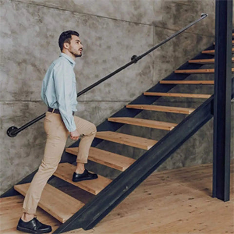 Sleek Black Wrought Iron Stair Rails With Super Grippy Non Slip Coating Zero Hassle Diy Wall Mount Setup Heavy Duty Indoor Outdoor Banister For Seniors Kids Hallway Loft And Bathroom 19 Feet Long used by a man climbing wooden stairs.