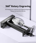 High Performance 360 Rotary Attachment For Laser Engraver Knocks Out Tubular Jobs Universal Fit Cups Bottles Tumblers Smooth Operator on a table with engraved glass.