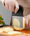 Front view of large crinkle cutter with stainless steel wavy blades and black handle slicing a potato on a cutting board.
