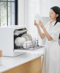 Woman loading plates into Flat Out Reliable Compact Countertop Dishwasher With Fully Automatic Smart Drying And Triple Wash Filter For Tiny Kitchens Or Rv Campers No Sweat Setup Easy Glide Rack Holds Massive Dinner Plates Built Different Quality.