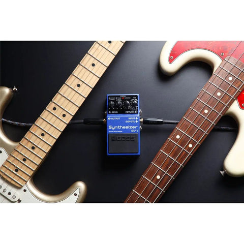 SY-1 Guitar and Bass Synth Pedal With Polyphonic Synth Engine between two guitars on a dark surface.