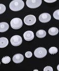 Grab This Awesome DIY Robot Gears And Pulley Belt Kit With 64 Kinds Of Wearable Plastic Parts Perfect For Tech Models, Car Robots, And Cool Motor Projects You Can Build Your Own Stuff With Today. white plastic gears on black background