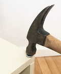 Hammer with a wooden handle removing a nail from a white piece of furniture on a wooden floor.