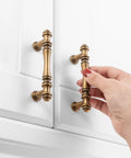 Hand holding 30 Pack 3 Inch Antique Brass Cabinet Pulls Set for Kitchen Cabinets, Drawers, Dressers and Cupboards on white door.