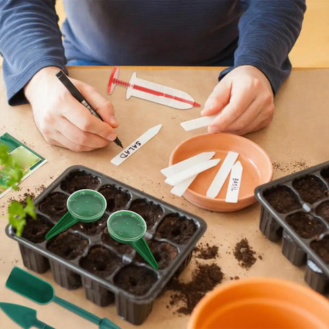 Person using 7 Piece Mini Seed Spreader Tool Set For Precise Seed Dispensing And Easy Garden Planting, labeling plant tags.