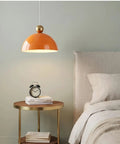 MIELPOXS Modern Dome Pendant Light Iron Metal Hanging Ceiling Fixture in orange above a bedside table with clock.