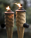 Close-up of two lit Bamboo Tiki Torches Outdoor Citronella Torches Weathered Color 4 Pack Large Patio Torches in a garden.