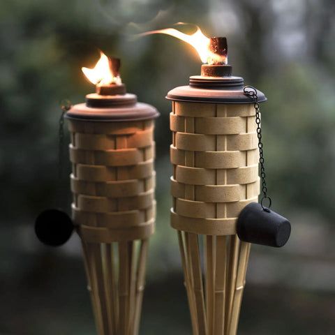 Close-up of two lit Bamboo Tiki Torches Outdoor Citronella Torches Weathered Color 4 Pack Large Patio Torches in a garden.