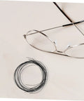 Eyeglass Repair Thread Cord For Half Rim Glasses Quick Fix Tool shown with wire thread next to silver half-rim glasses on a beige surface
