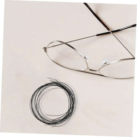 Eyeglass Repair Thread Cord For Half Rim Glasses Quick Fix Tool shown with wire thread next to silver half-rim glasses on a beige surface