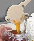 White plastic honey gate valve with lever, honey pours into a glass jar