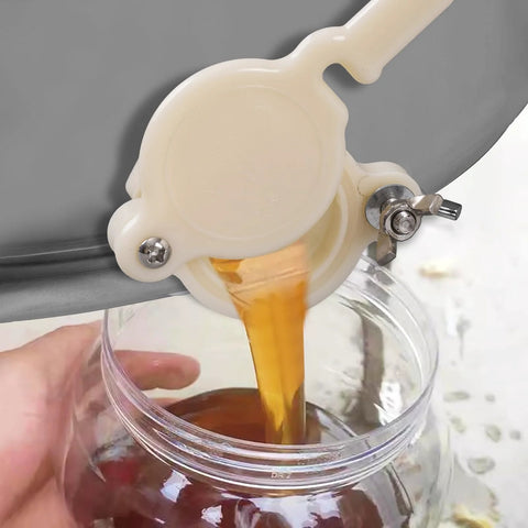 White plastic honey gate valve with lever, honey pours into a glass jar