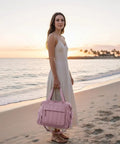 Woman on beach at sunset holding a pink insulated soft travel duffel bag. Crush The Summer Heat With This Snazzy Puffer Cooler Bag Stowing 35 Frosty Drinks Inside An Insulated Soft Travel Duffel Crafted For Pink Tailgates And Beach Days.