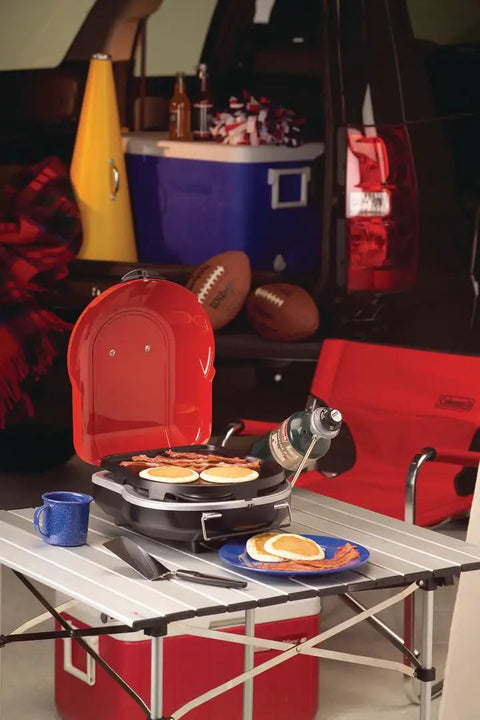 Fold N Go 6000 BTU Portable Propane Grill With InstaStart Push Button Starter on a table at a tailgating event