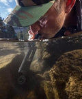 Person using Peak Series Personal Water Filter Straw for Backup Filtration and Emergency Survival Outdoors in a stream.