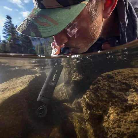 Person using Peak Series Personal Water Filter Straw for Backup Filtration and Emergency Survival Outdoors in a stream.