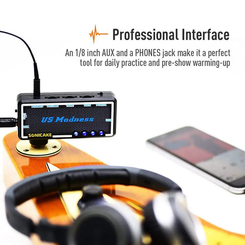Close-up of Guitar And Bass Headphone Amp With Built In Chorus Effects Portable Rechargeable Mini Headphone Amplifier For Silent Practice Great For On The Go Includes Headphone Splitter And One Eighth Inch Aux Cable with headphones and smartphone in background.