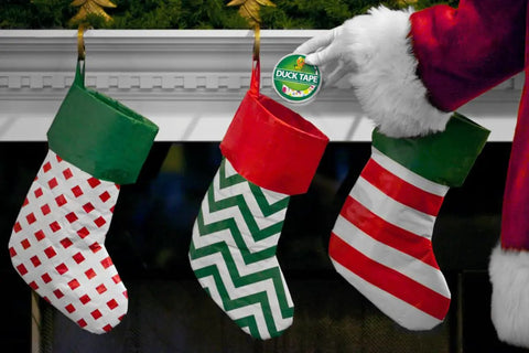 Santa placing Heavy Duty White Duct Tape 3 Pack in stocking, three festively patterned stockings on mantel, Christmas theme.