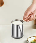 Hand holding Turkish Coffee Pot Stainless Steel Multipurpose Milk Frothing Pitcher And Coffee Kettle For Office Kitchen Home Bar 600ml Durable Spout With Wooden Handle Ideal For Latte Art