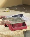 Heavy Hitter 7 Inch Wet Tile Saw With Rust Proof Stainless Top And Adjustable Rip Fence For Smooth Cuts On Ceramic Porcelain And Stone Featuring A Water Tray That Keeps Blades Cool And Slashes Dust During Weekend Remodel Tasks in use with a tile being cut.