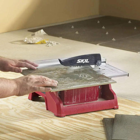 Heavy Hitter 7 Inch Wet Tile Saw With Rust Proof Stainless Top And Adjustable Rip Fence For Smooth Cuts On Ceramic Porcelain And Stone Featuring A Water Tray That Keeps Blades Cool And Slashes Dust During Weekend Remodel Tasks in use with a tile being cut.
