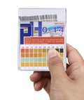 Hand holding Ultra Accurate pH Test Strips 0-14 With 0.5 Precision, 100 Strips Litmus Paper for acid alkaline readings.