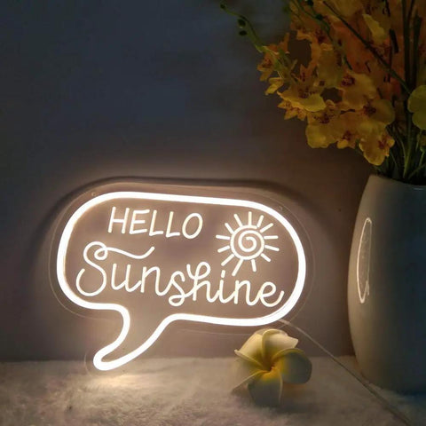 Sunshine Neon Sign For Wall Decor LED Light Up Sign For Bedroom Office Kids Room Nursery Living Room 12.2 By 9 Inches Warm White Glow Lit Vibe Great Perfect Birthday Gift For Girls And Boys showing 'Hello Sunshine' in warm white glow next to a vase with yellow flowers.
