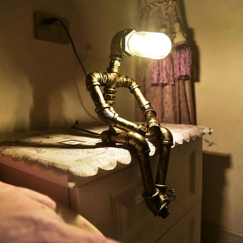 Steampunk Table Lamp With Robot Pipe Design In Bronze Industrial Desk Light For Office Bedroom And Living Room Vintage Retro Dope Loft Style Space That Adds A Cozy Industrial Glow For Any Room. Unique sitting robot design on a bedside table.