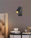 Modern Rotatable Cylinder Wall Sconce Wall Mount Reading Spotlight in black on a gray wall, illuminating a bedside area.