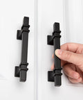 Hand holding 10 Pack 3 Inch Matte Black Cabinet Pulls With Solid Steel Construction And Zinc Alloy Base on white cabinet