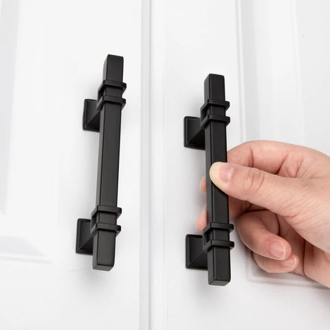 Hand holding 10 Pack 3 Inch Matte Black Cabinet Pulls With Solid Steel Construction And Zinc Alloy Base on white cabinet