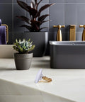 Copper Bathtub Drain Stopper with Bounce Design for Easy Control on marble countertop next to potted plants in modern bathroom setting.