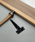 Close-up of a black hinge from an 8-piece galvanized T-strap hinges set for barn doors and outdoor wood gates on a table.