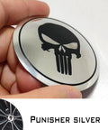 Four Piece Heavy Duty Aluminum Hub Center Cap Decals Featuring Dope Tusked Skull Art For Clean Wheel Cover Stickers That Slap Onto Most Standard Rims Smoothly, showing shiny silver skull cap decal held in hand.