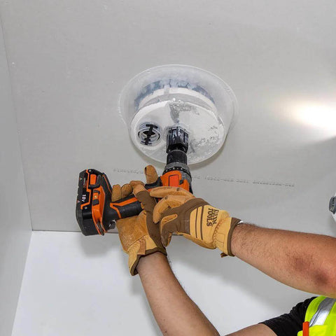 Klein Tools 53710 hole saw attached to orange cordless drill cutting drywall ceiling tile with integrated dust bowl