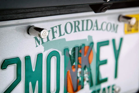 Close-up of a 45 caliber license plate screw featuring a bullet fastener on a car's registration plate.