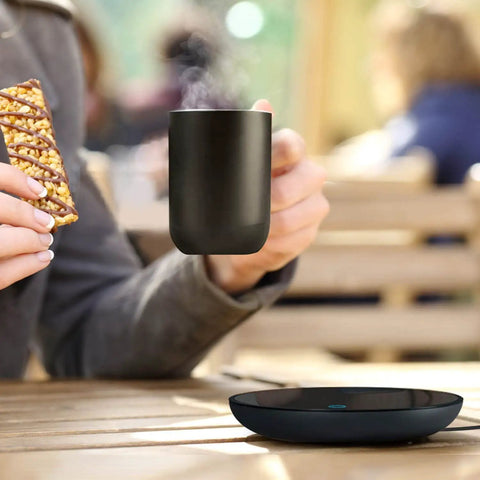 Smart Electric Coffee Mug Warmer With Dual Temperature Settings And Auto Shut Off Keeps Your Daily Brew Absolutely Fire All Day Long The Ultimate Desk Essential For Hot Coffee Tea Or Milk in use outdoors with a black mug and snack.