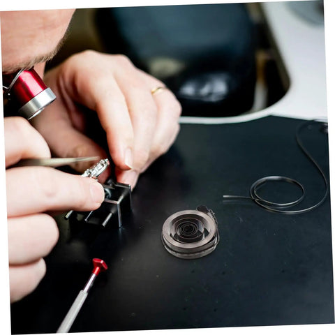 Person using tools from Vintage Mechanical Alarm Clock Repair Kit With Precision Steel Parts And Winding Key on black workbench.
