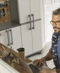 Man sitting at desk with laptop, Built Tough Resin Storage Cabinet With Lockable Doors And Five Shelves in background