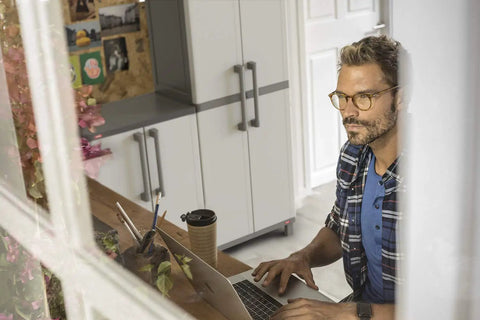 Man sitting at desk with laptop, Built Tough Resin Storage Cabinet With Lockable Doors And Five Shelves in background
