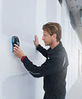 User operating the Road Ready 5 In 1 Wall Scanner And Electronic Stud Sensor on a wall to locate hidden materials.