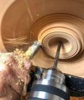 Close-up of a stainless steel carbide wood lathe detailer tool, unhandled, cutting inside a spinning wooden bowl.