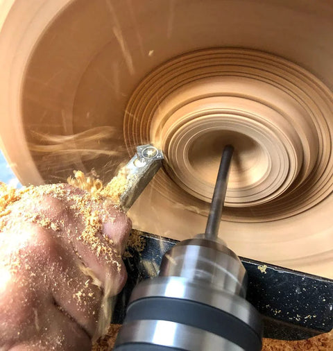 Close-up of a stainless steel carbide wood lathe detailer tool, unhandled, cutting inside a spinning wooden bowl.
