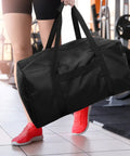 Person carrying Mid-Size Weekender Travel Duffle Bag, 24x12x12 Inch, 53L Capacity, Water Resistant Black Duffel For Overnight Trips